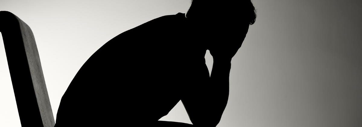 The silhouette of a man sitting in a chair, holding his face in his hands, clearly depressed